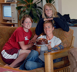 Three teens on the couch with a cake and candles