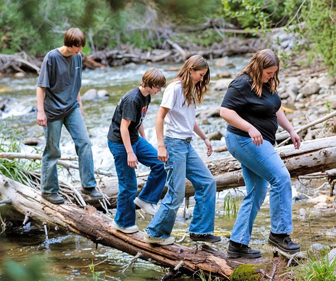 Four young adults crossing on logs over a creek