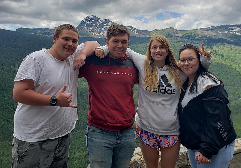Four friends arm-in-arm with beautiful mountains and blue sky, white clouds