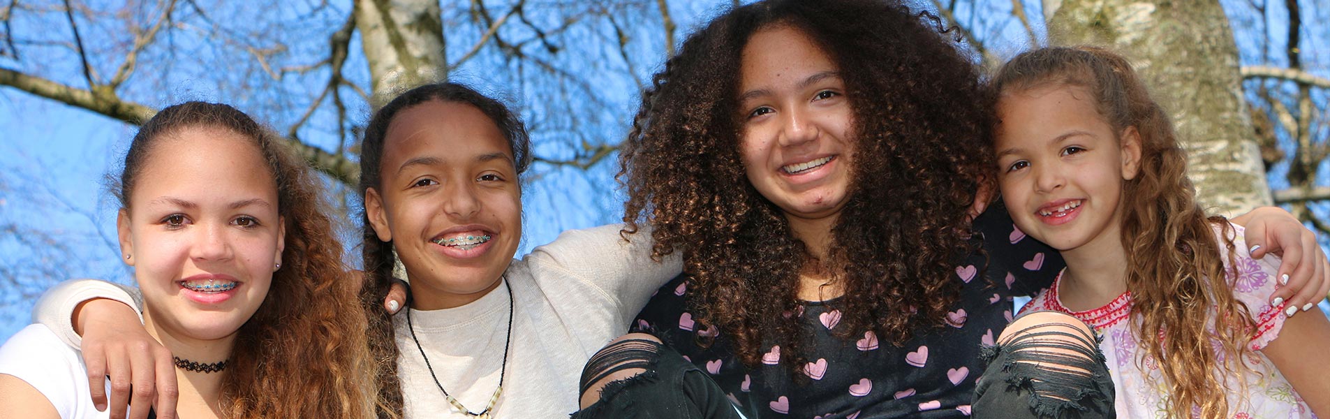 Four young adults smiling at camera arm in arm