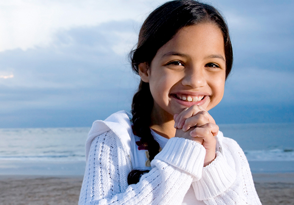 Little girl with hands folded and under chin, ocean behind her